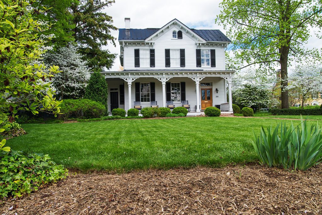 A two-story white farmhouse with green grass and surrounded by trees.